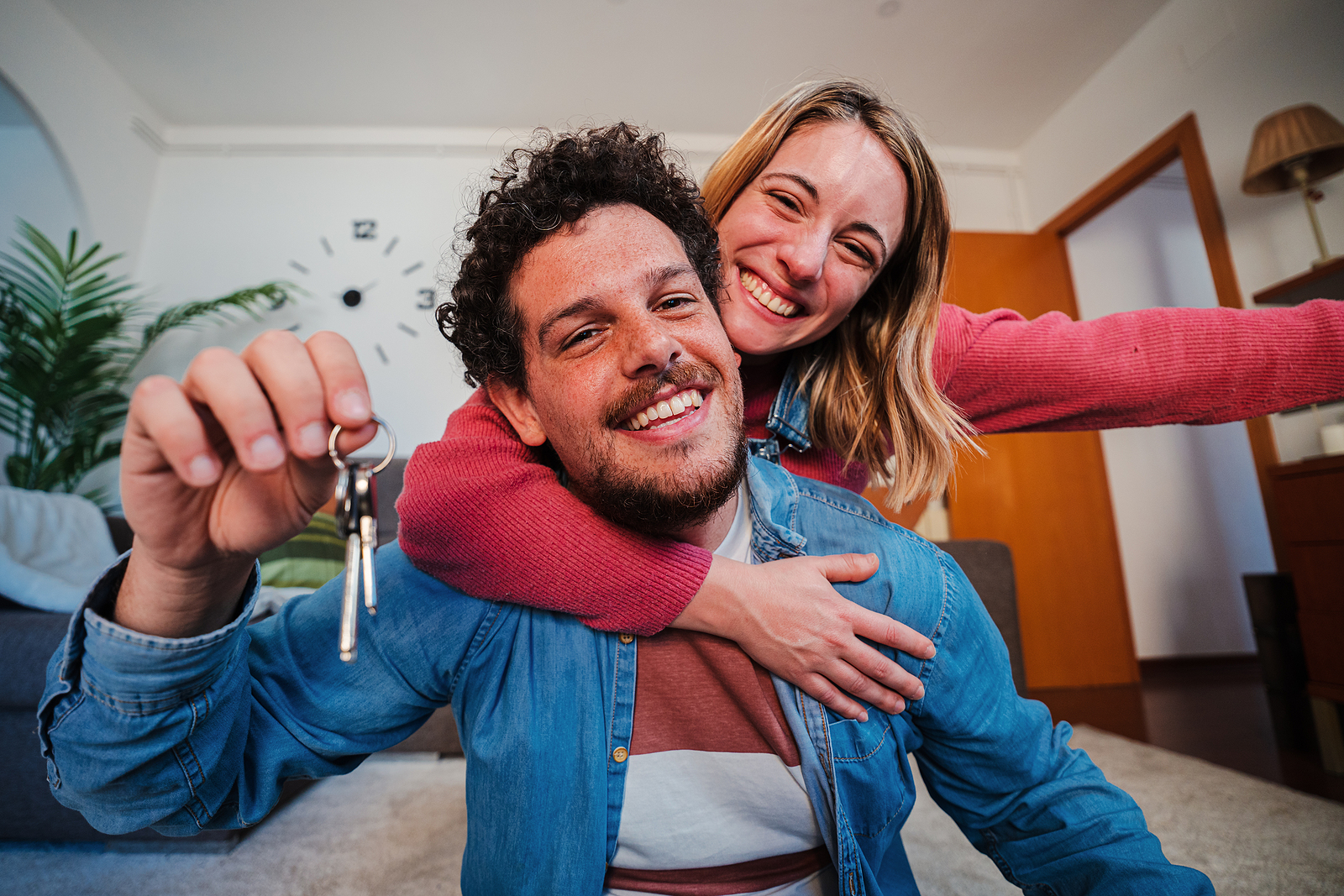 Young caucasian couple showing keys of their first house after purchase and moving to new home together. happy husband and wife hugging in their apartment excited to be owners of a apartment.