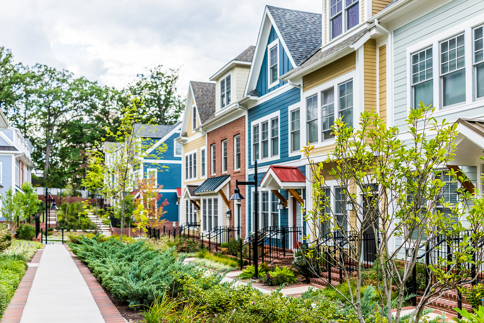 Row of colorful red yellow blue white green painted residential townhouses homes houses with brick patio gardens in summer