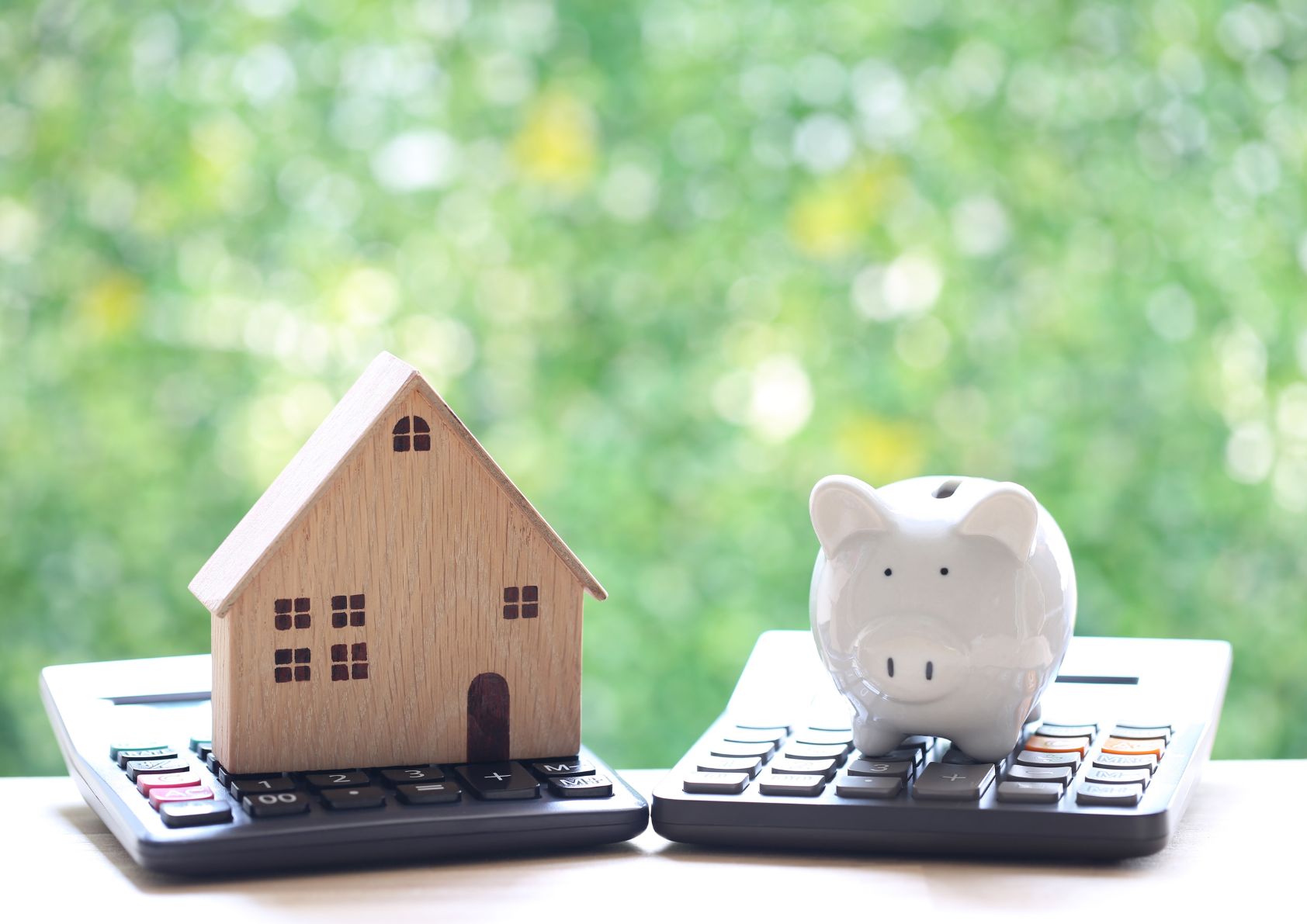 Home equity depiction with a wooden small house and piggy bank sitting on top of handheld calculators