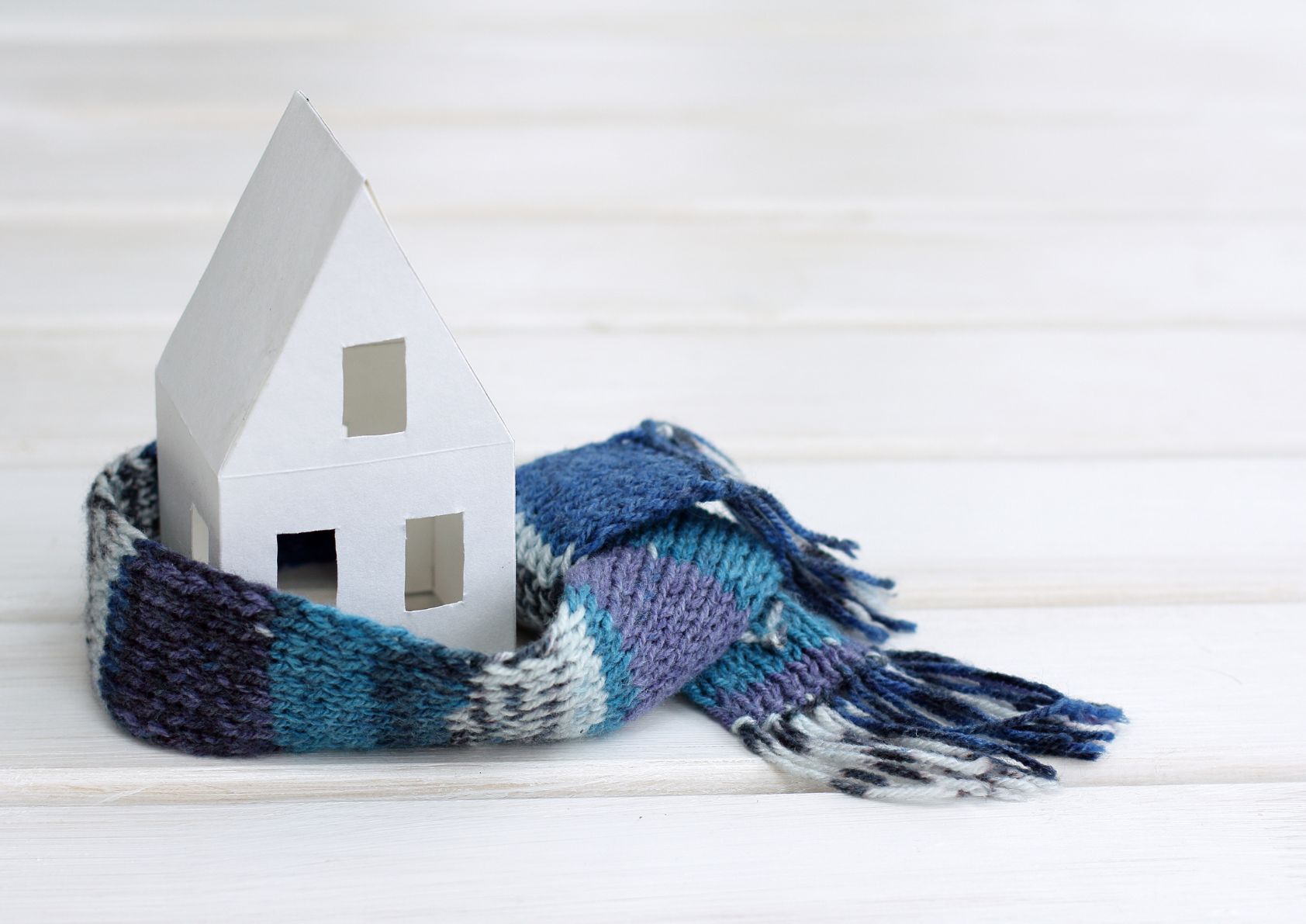 Tiny model home wrapped in a scarf. Depicting a home in winter