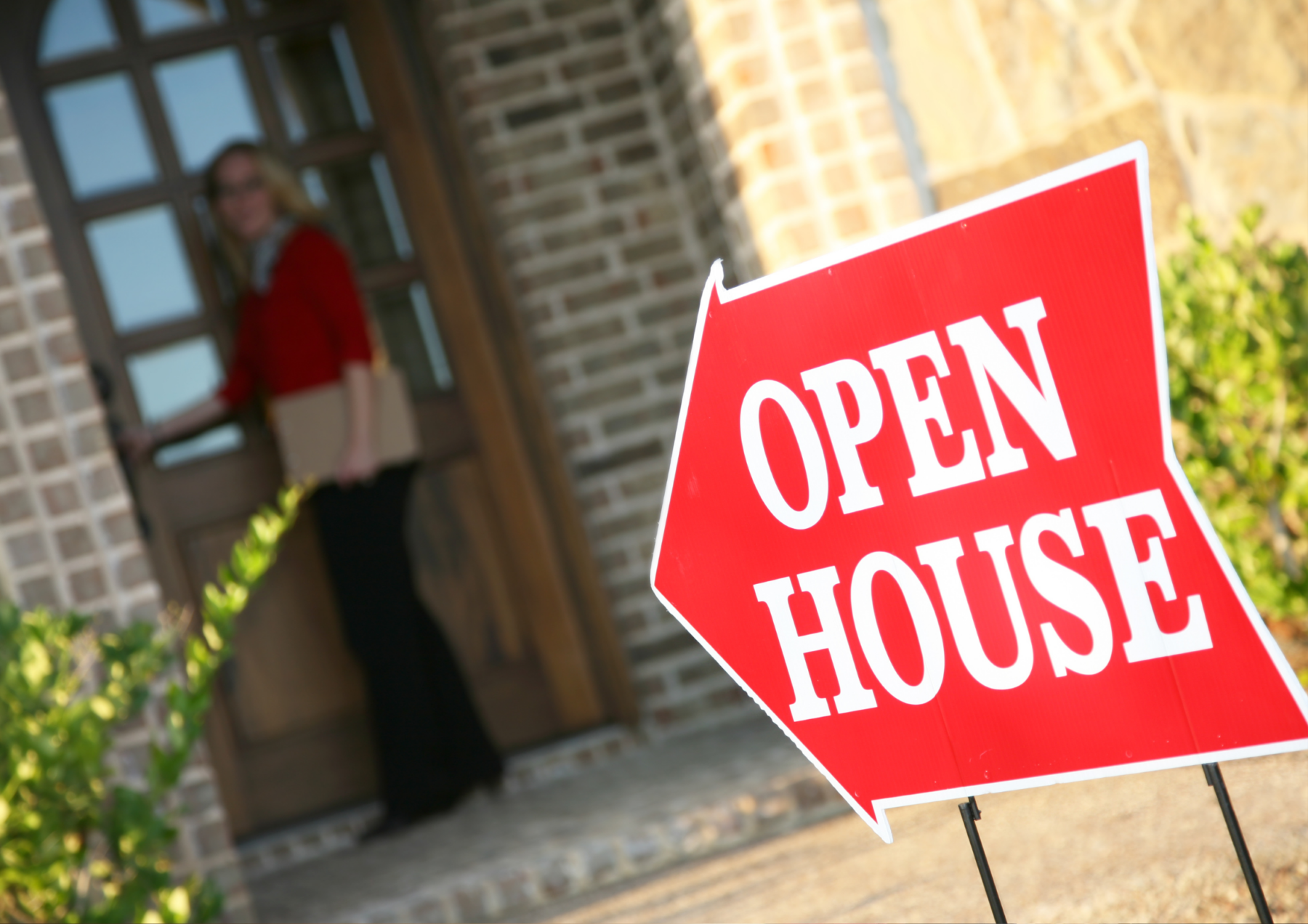 Open house sign pointing to a door with a lady standing in front of it. 